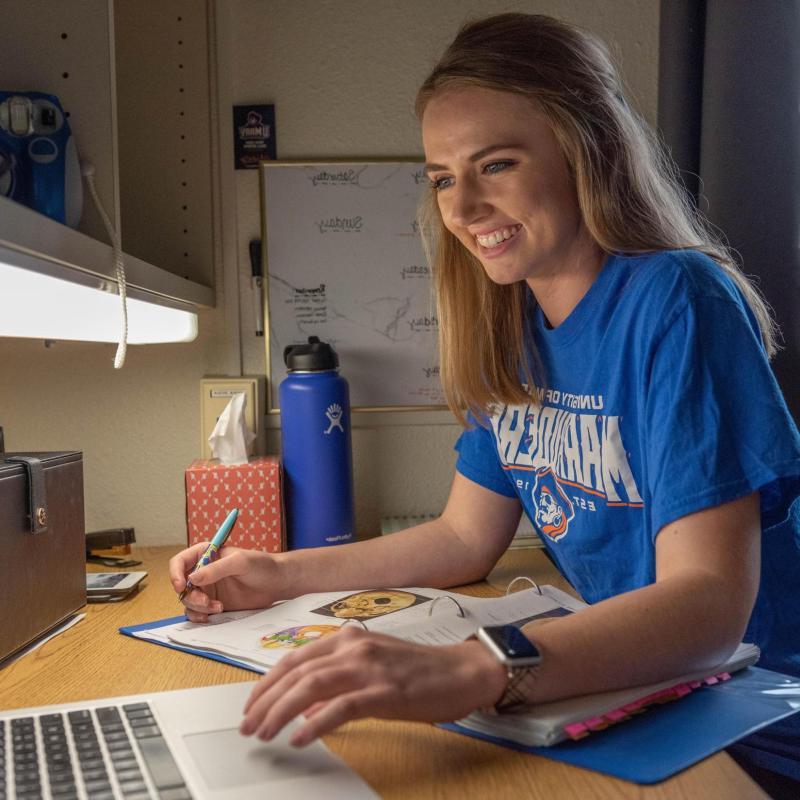 Female student typing on laptop in her residence hall.